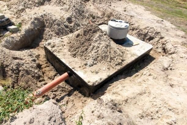 Septic tank partially buried in sand with an access lid and inlet pipe.