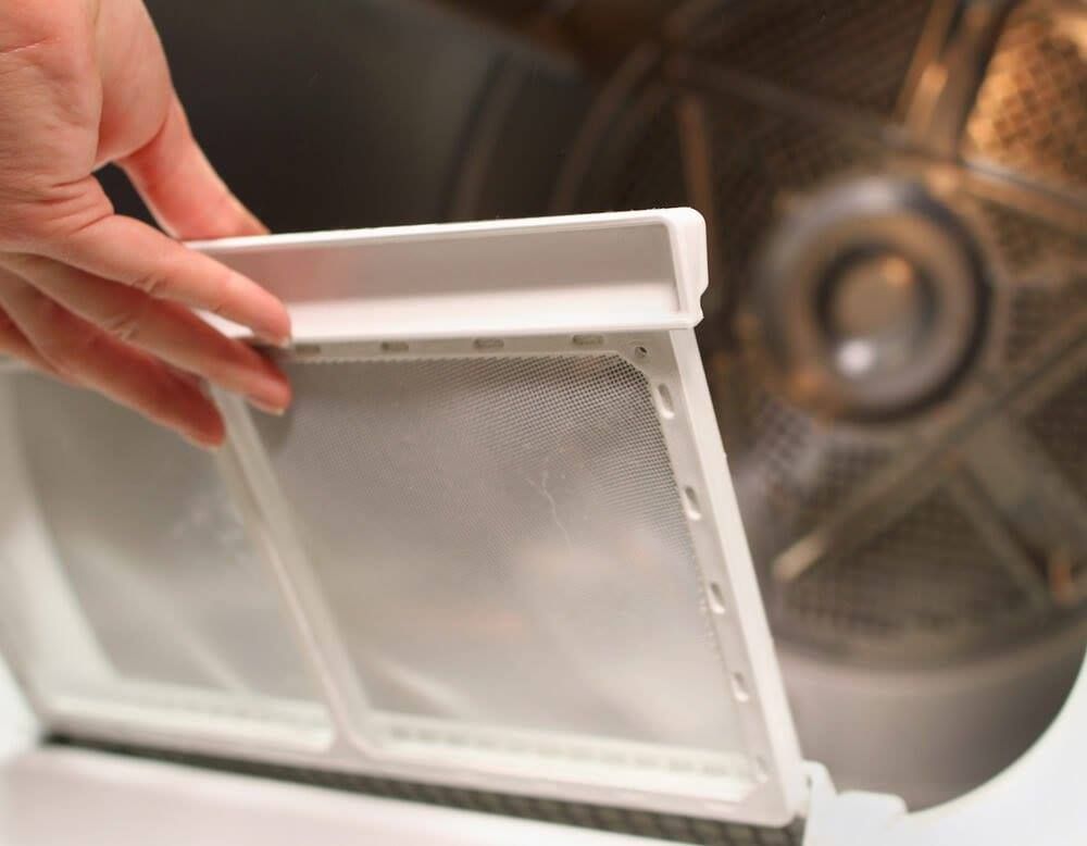 Hand removing lint filter from a clothes dryer, showing the mesh screen.