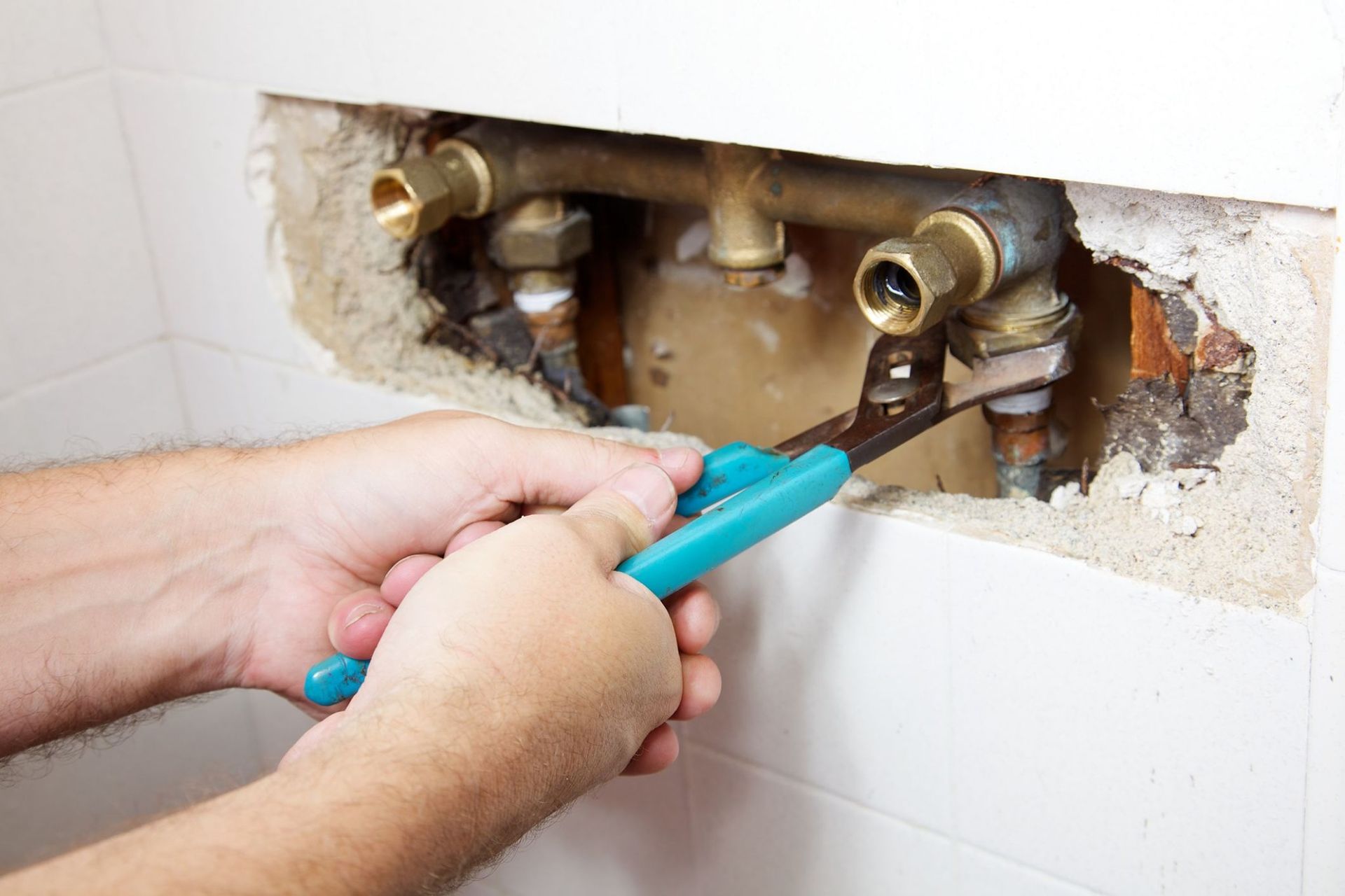 Plumber using pliers to tighten a brass pipe fitting in a bathroom wall.