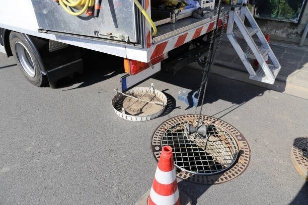 A maintenance truck next to an open manhole on a paved street with a cone and equipment.