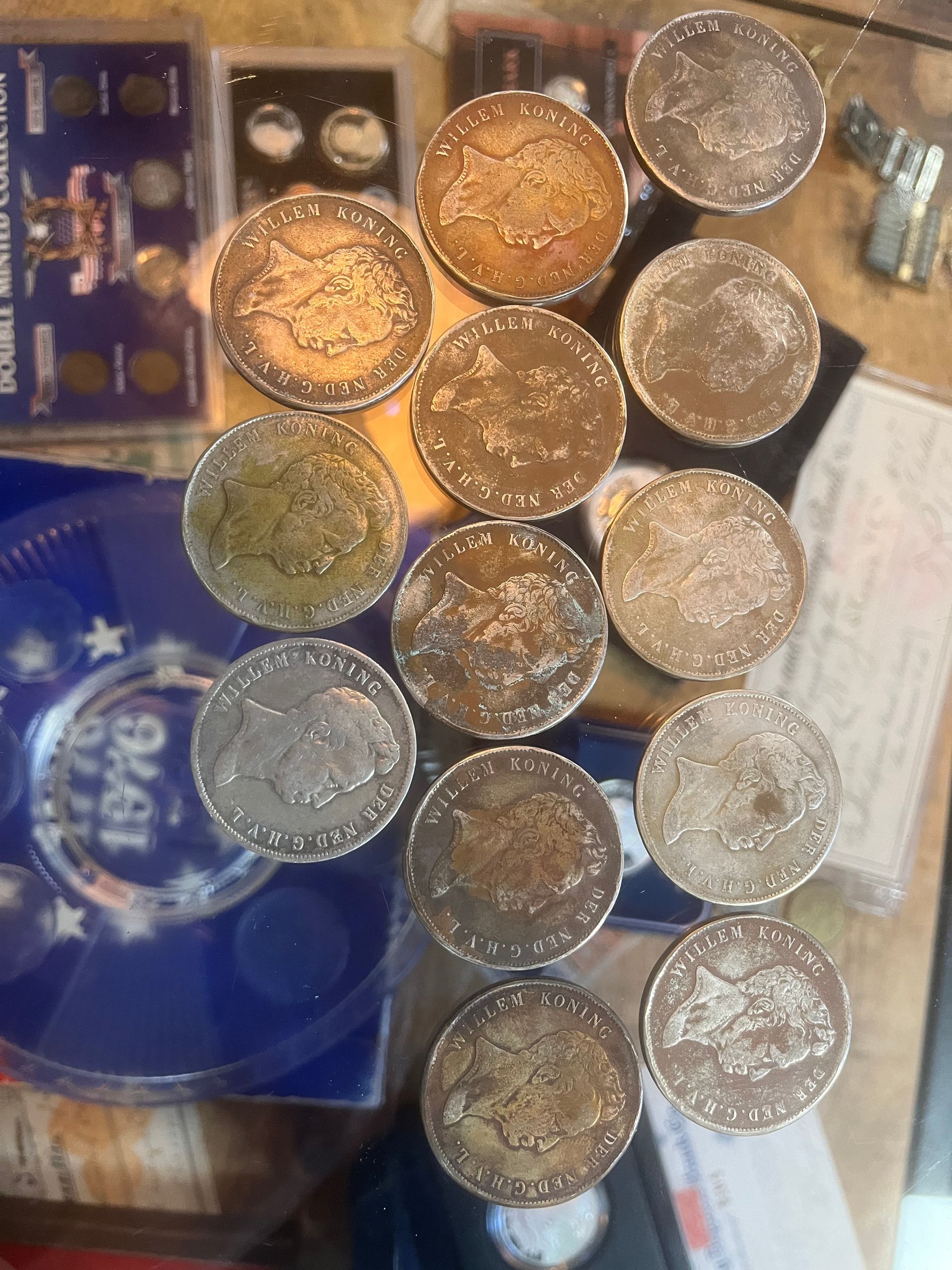 A collection of silver-colored coins arranged in a loose, vertical grouping on a surface near various coin display cases.