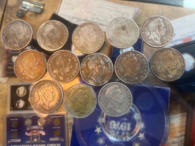 A collection of silver-colored coins arranged in a loose, vertical grouping on a surface near various coin display cases.