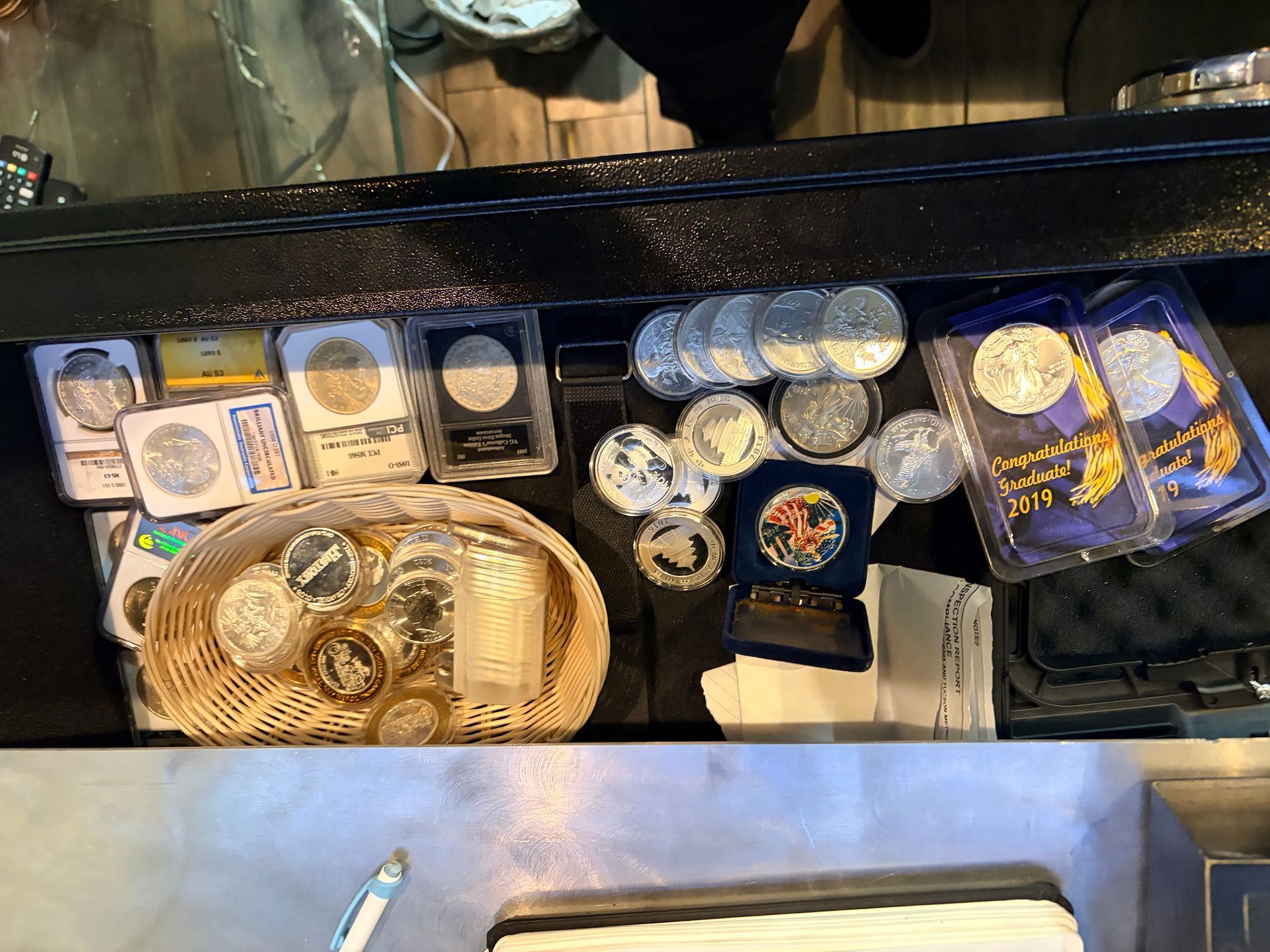 A high-angle shot of a collection of various silver coins, some in protective cases and others inside a small wicker basket.