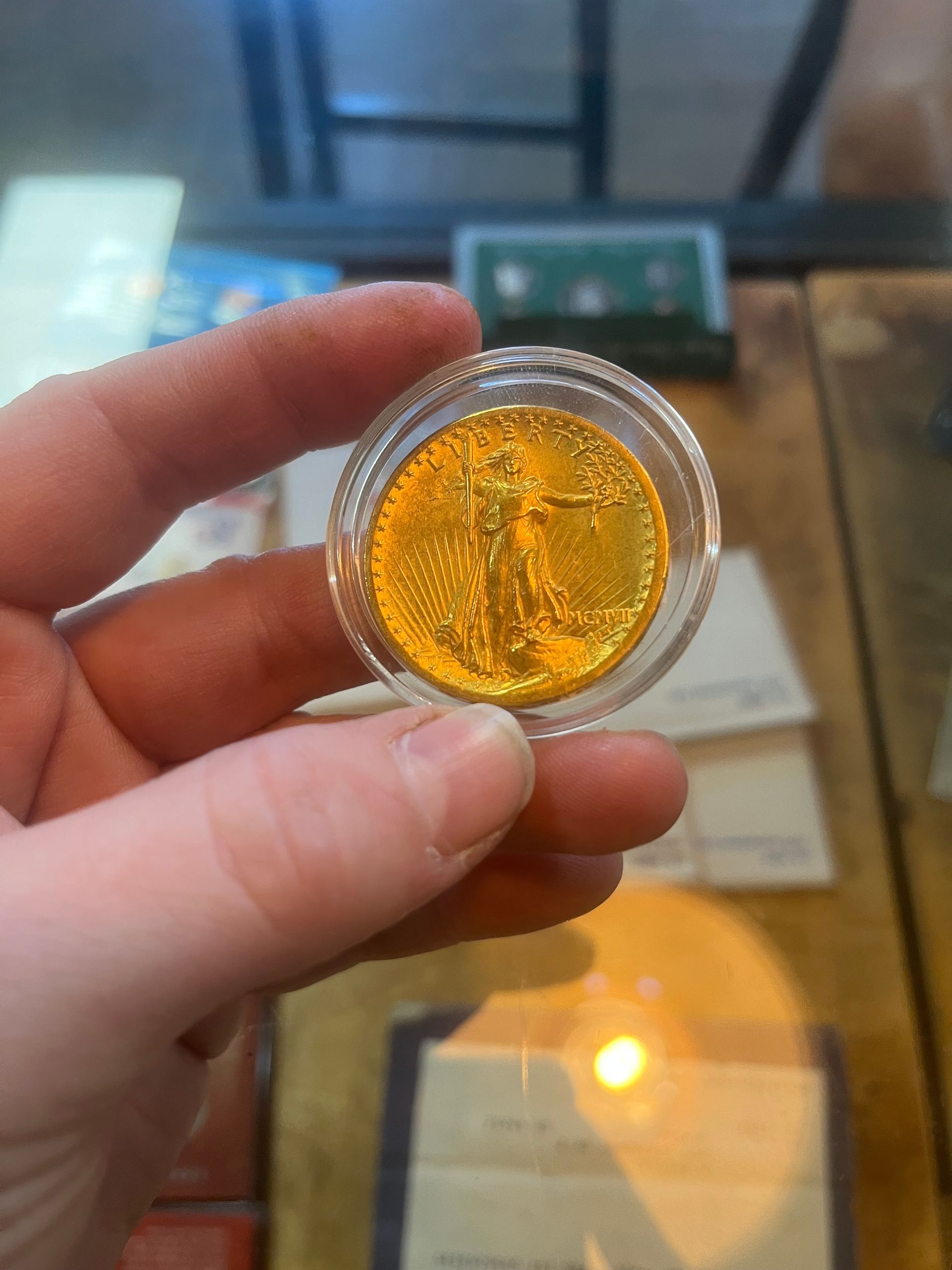 A person holds a small, brilliant gold coin encased in a clear plastic protective capsule.