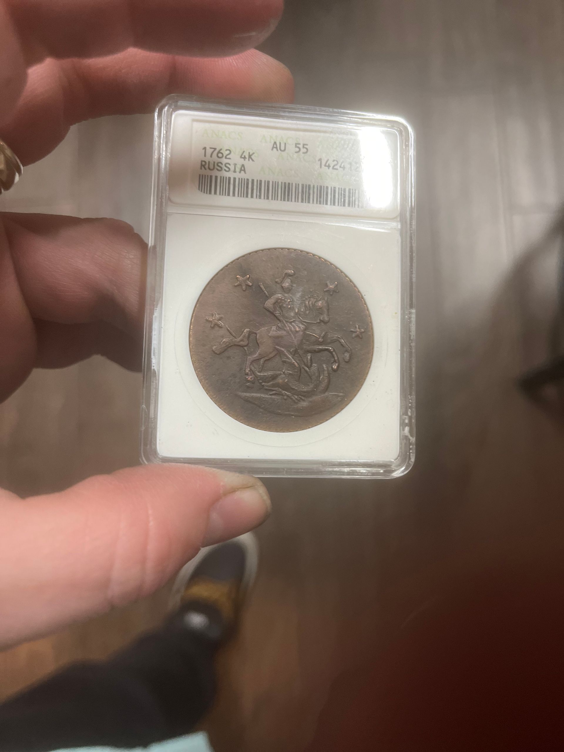 A hand holds a slabbed 1887 Great Britain sovereign gold coin featuring Saint George slaying the dragon.