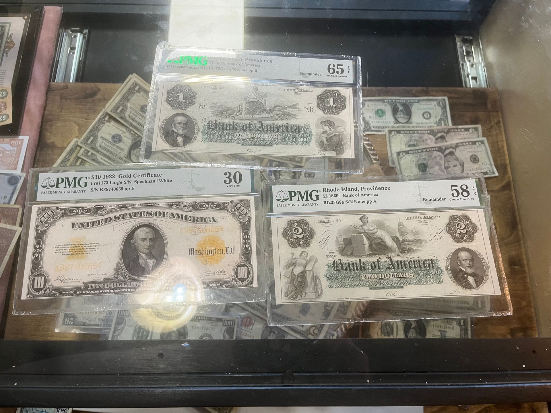 Three graded vintage US paper currency notes displayed in protective plastic cases inside a glass display case.