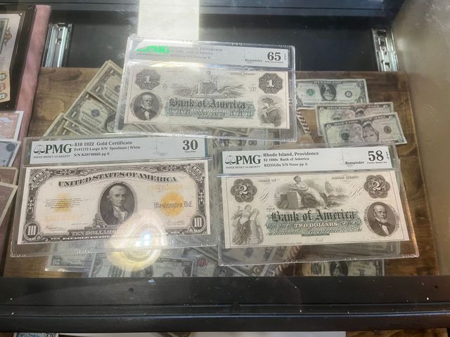 Three graded vintage US paper currency notes displayed in protective plastic cases inside a glass display case.