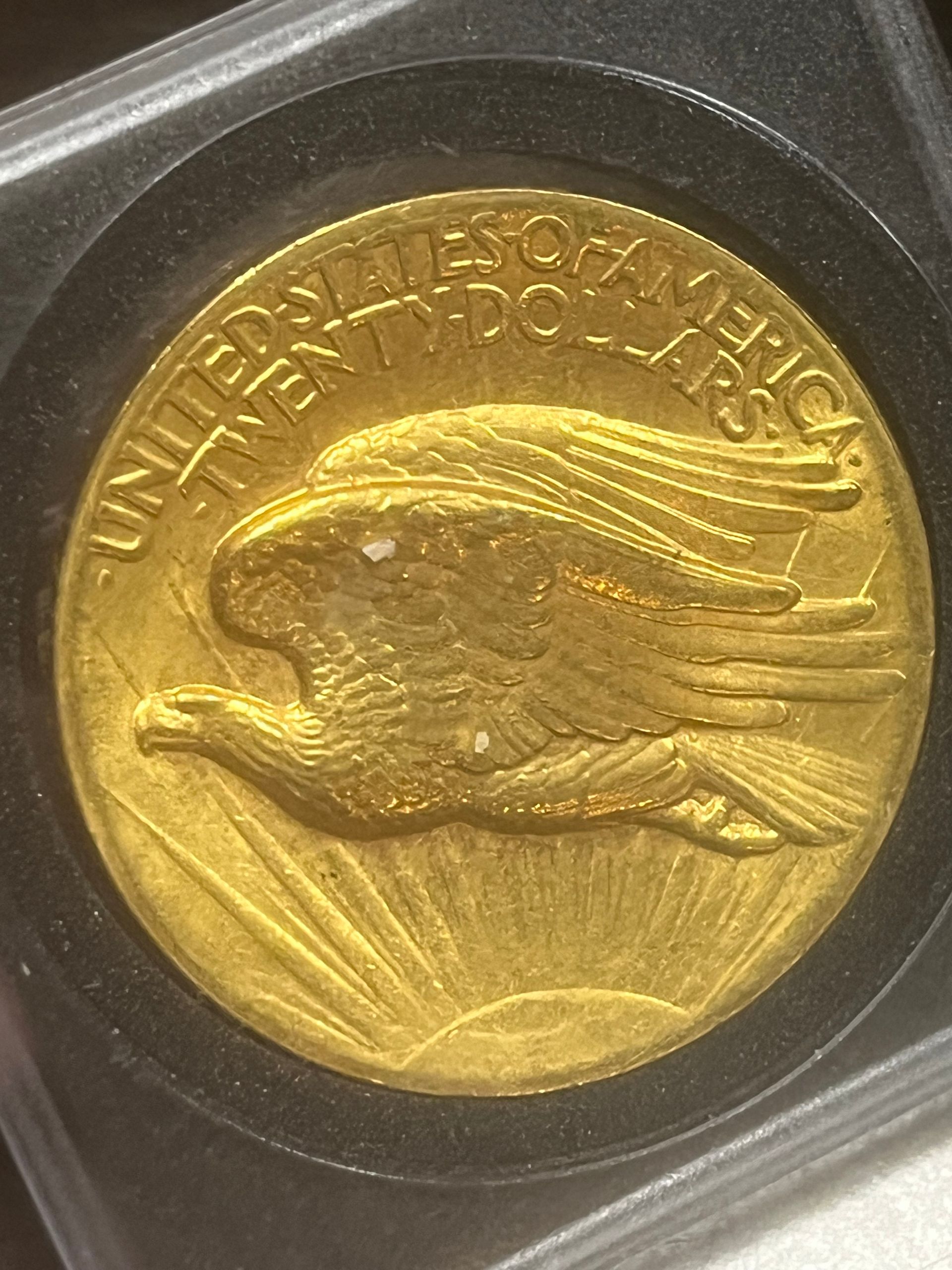 A gold Saint-Gaudens double eagle coin features an eagle in flight over a rising sun within a protective display case.