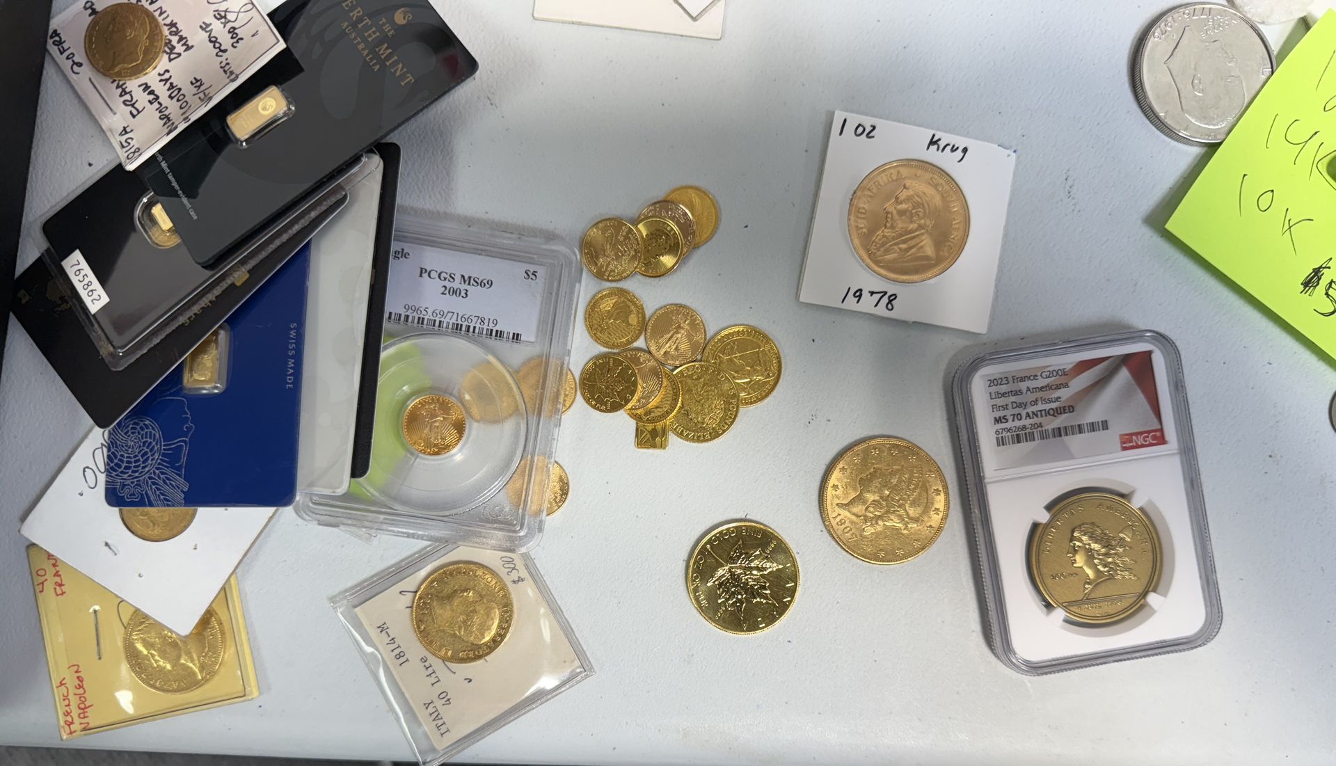 A collection of gold coins and small gold bullion bars displayed on a white surface, including some in protective cases.