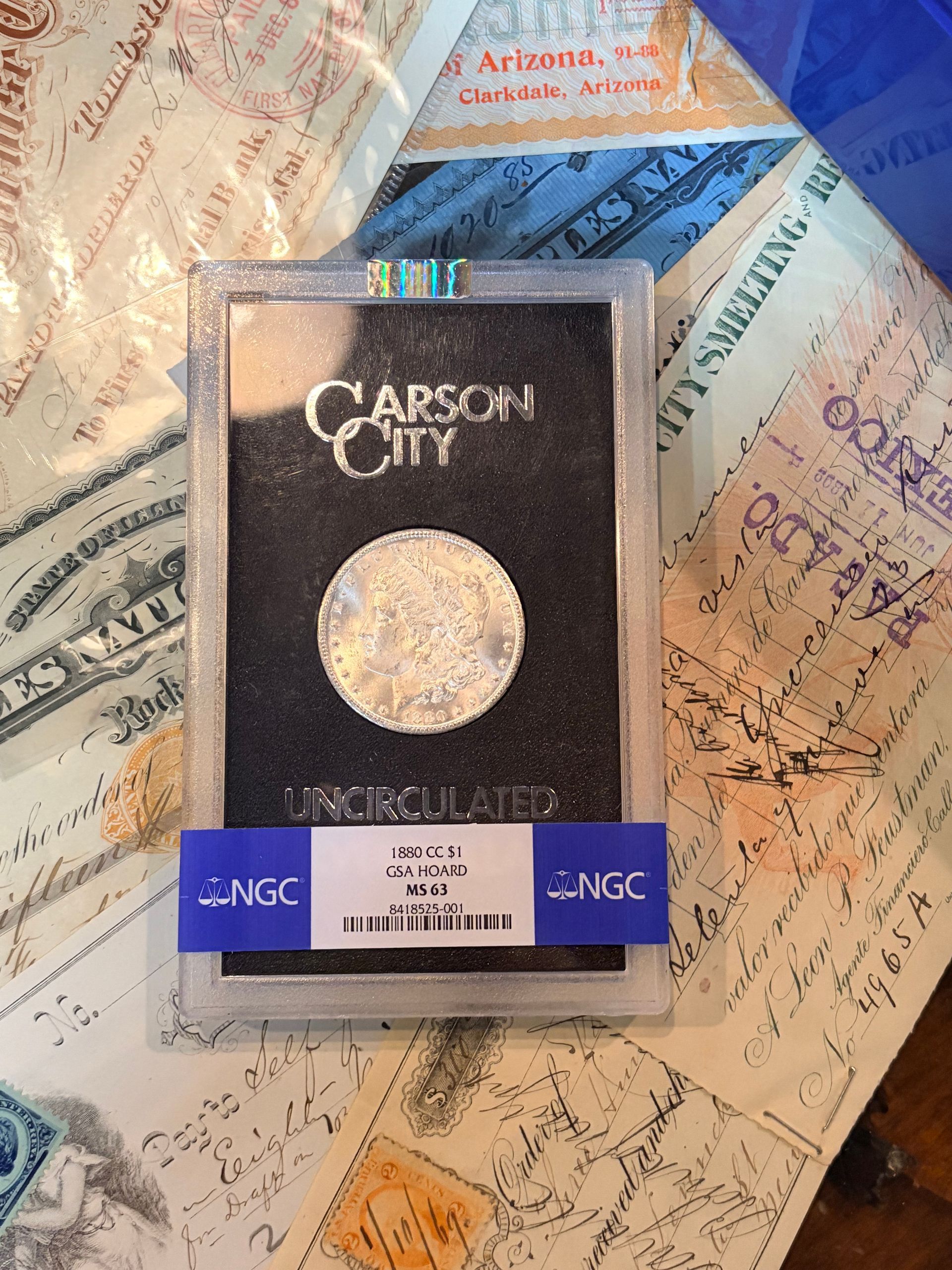 A GSA-slabbed Carson City Morgan silver dollar in a plastic holder with an NGC band, resting on a vintage document surface.