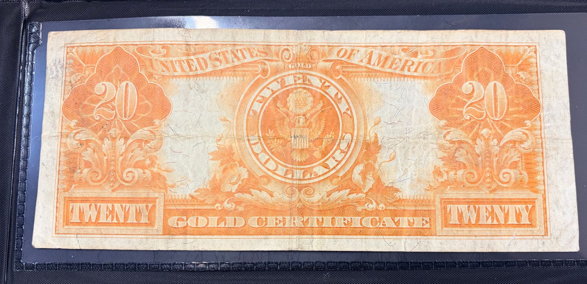 A rectangular orange-toned United States twenty-dollar gold certificate bank note with ornate borders and central seal.