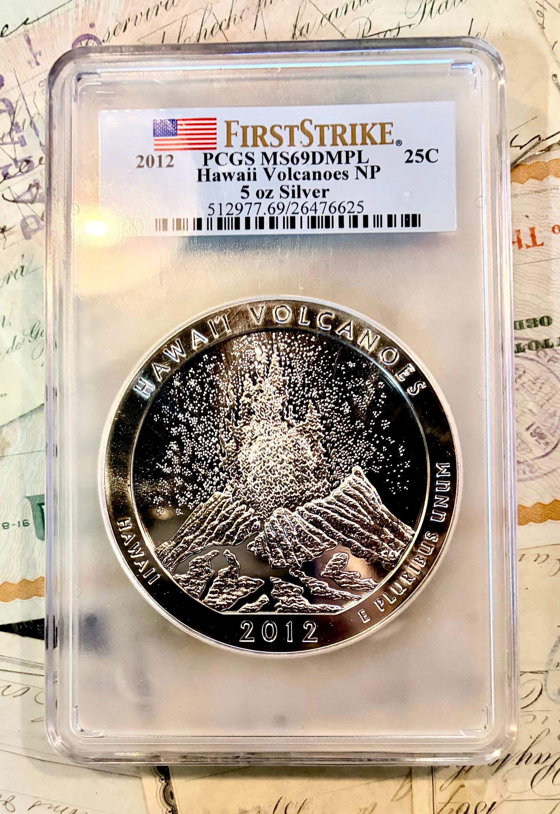 A 2012 Hawaii Volcanoes National Park 5 oz silver coin in a PCGS First Strike slab, featuring an erupting volcano.