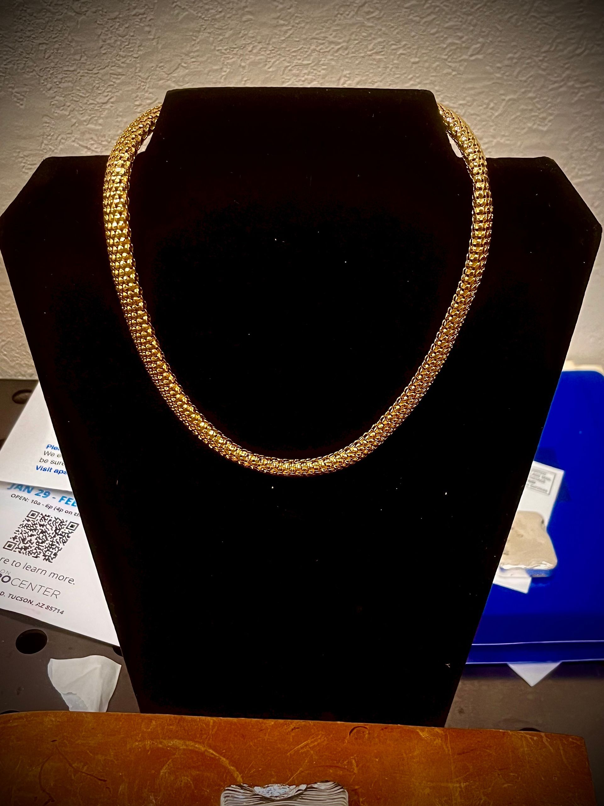 A gold-colored, textured, round chain necklace displayed on a black velvet mannequin bust.