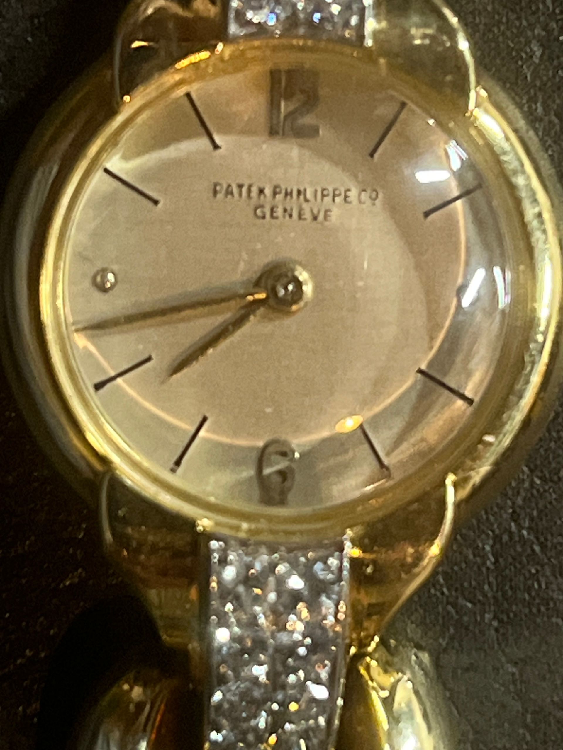 A close-up view of a gold Patek Philippe Geneve women's wristwatch with a round face and a diamond-encrusted bracelet.