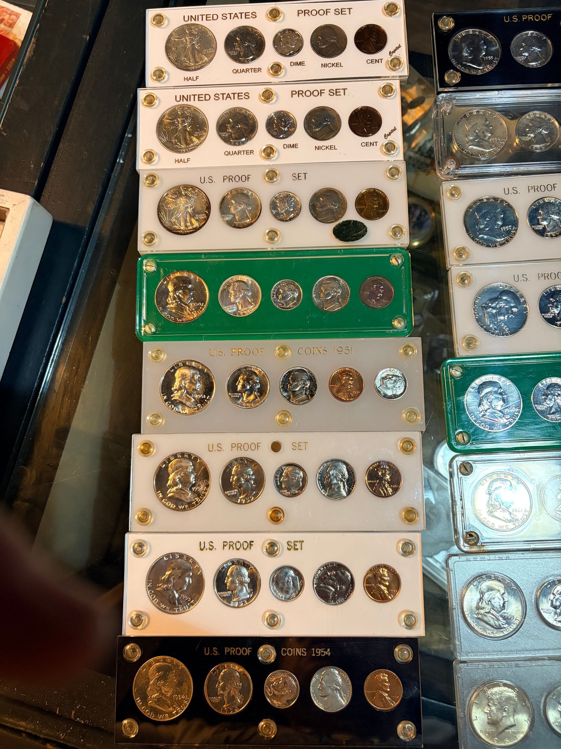 A vertical stack of U.S. coin sets in protective plastic holders, arranged by year on a dark surface.
