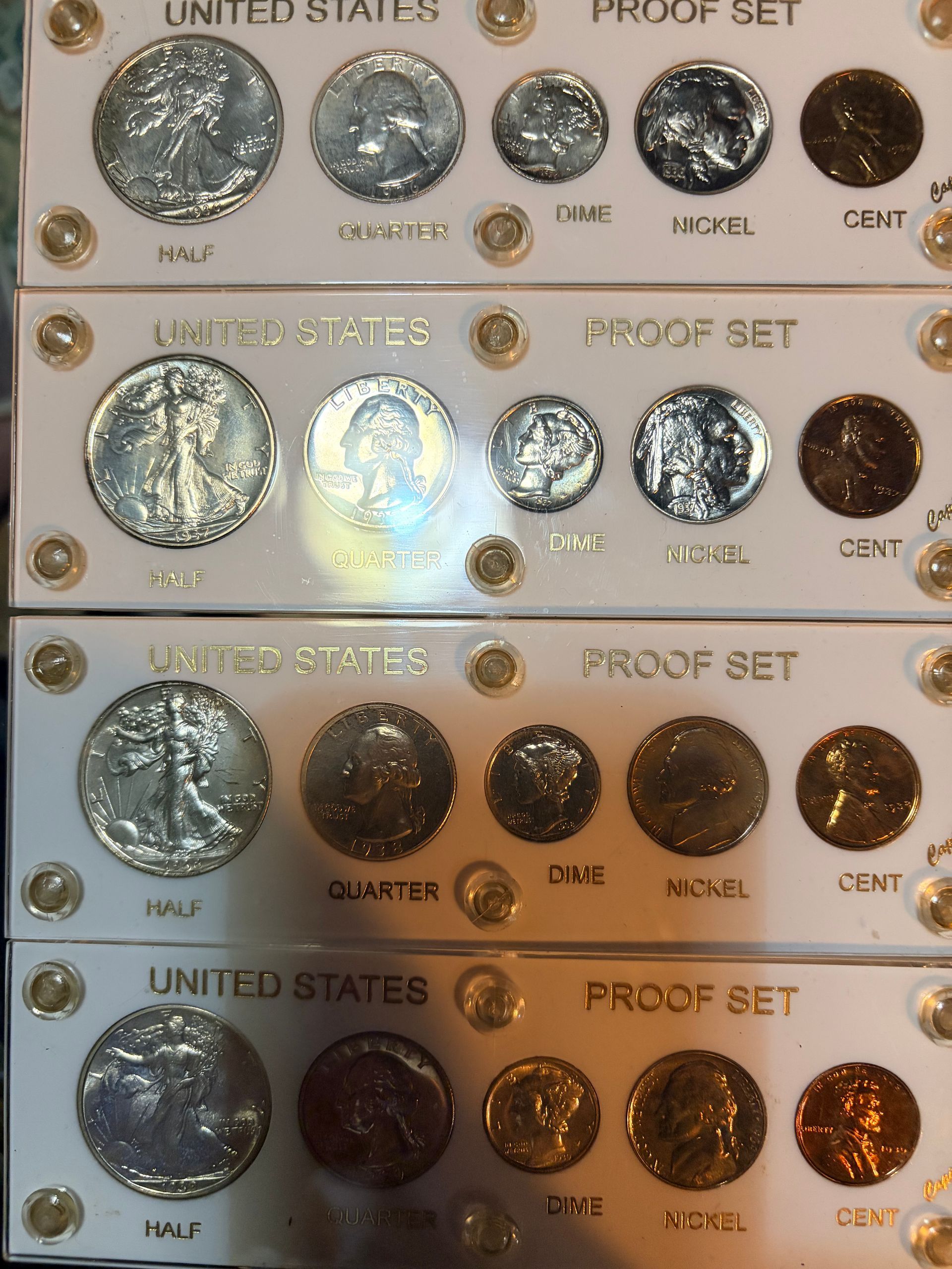 Four stacked plastic cases, each containing a United States Proof Set of five coins: half dollar, quarter, dime, nickel, cent.