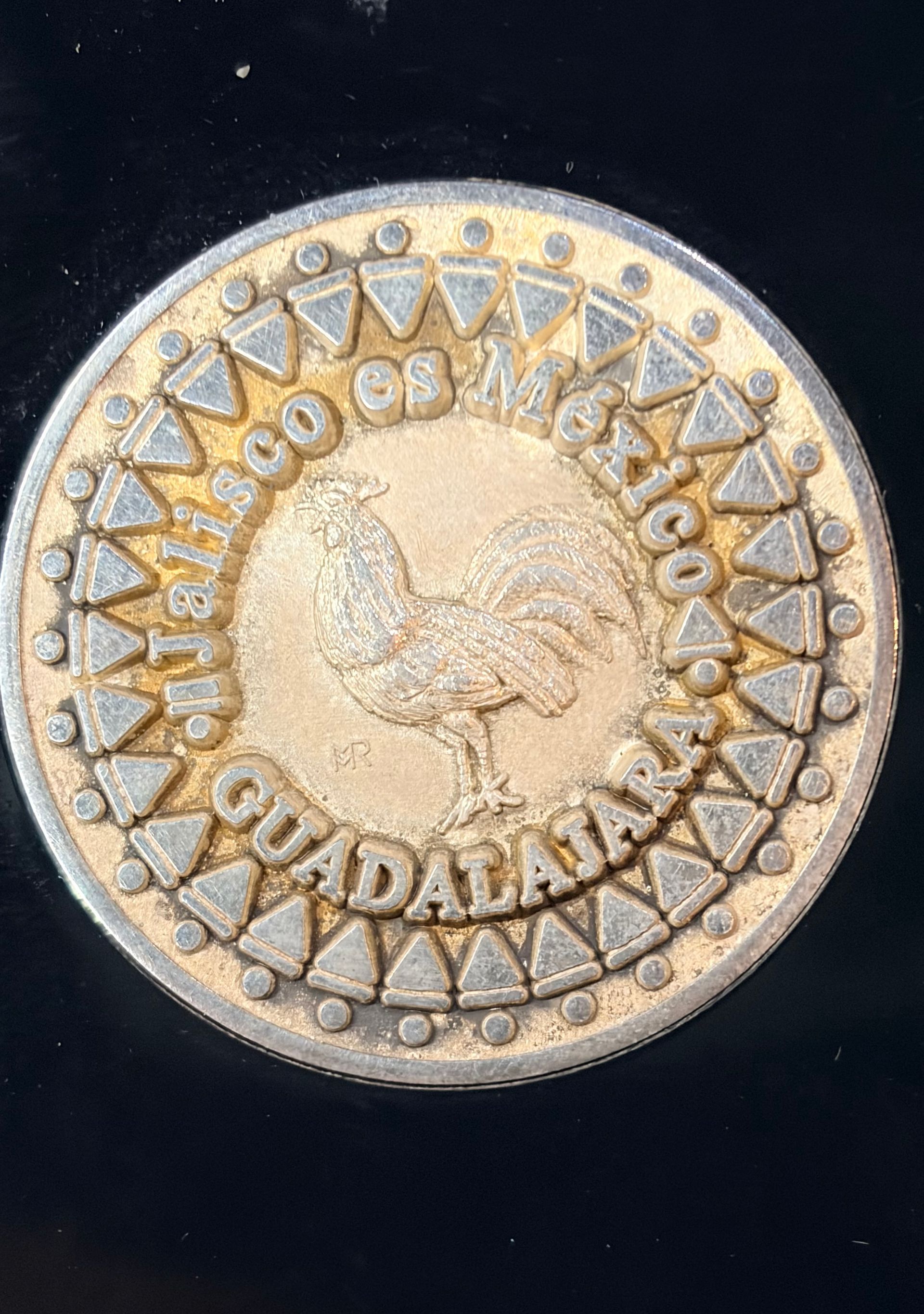 A round metallic coin featuring a rooster in the center, surrounded by the text Jalisco, Mexico and Guadalajara.