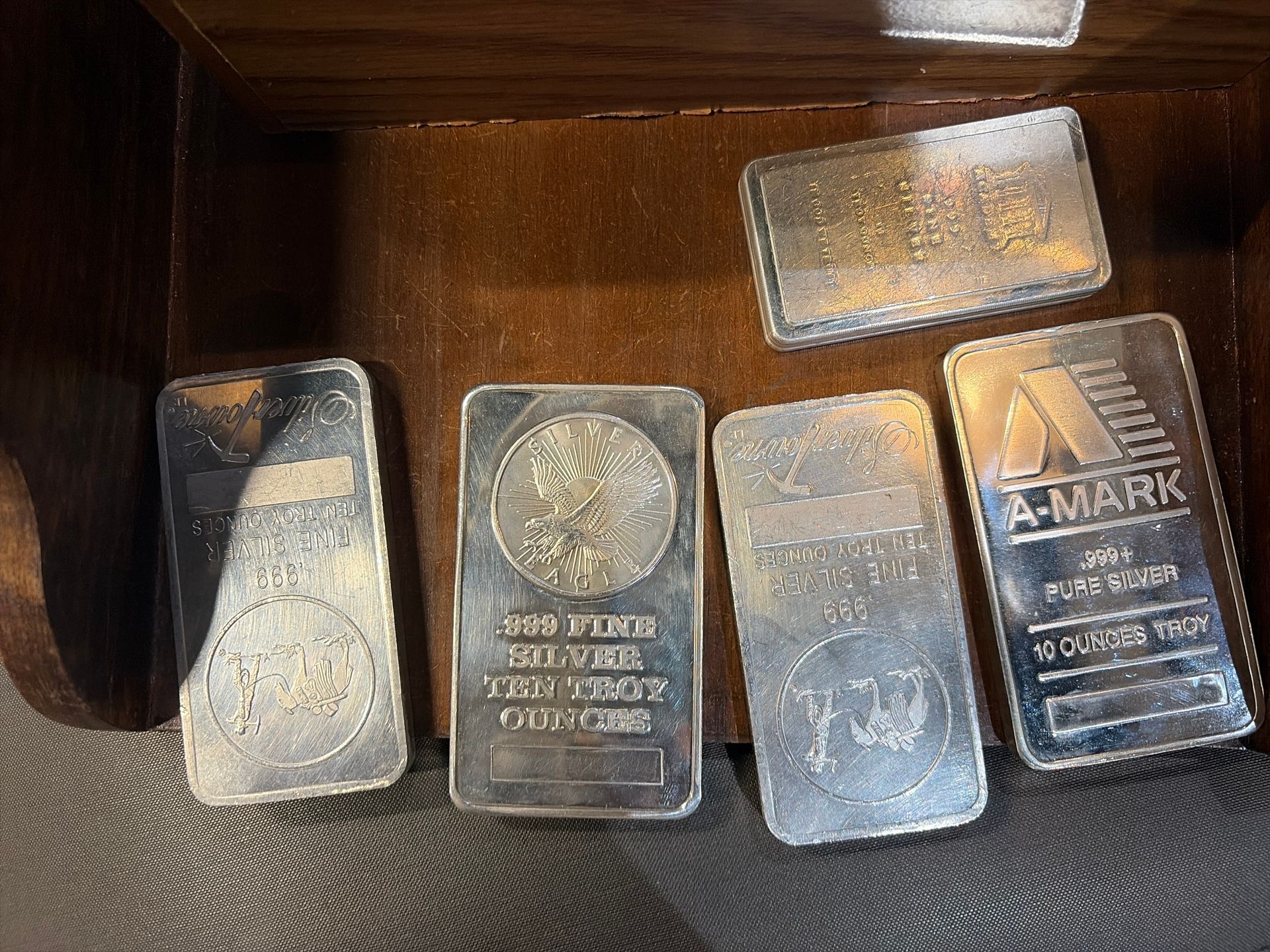Five rectangular silver bars with various mint markings, arranged inside a wooden container.