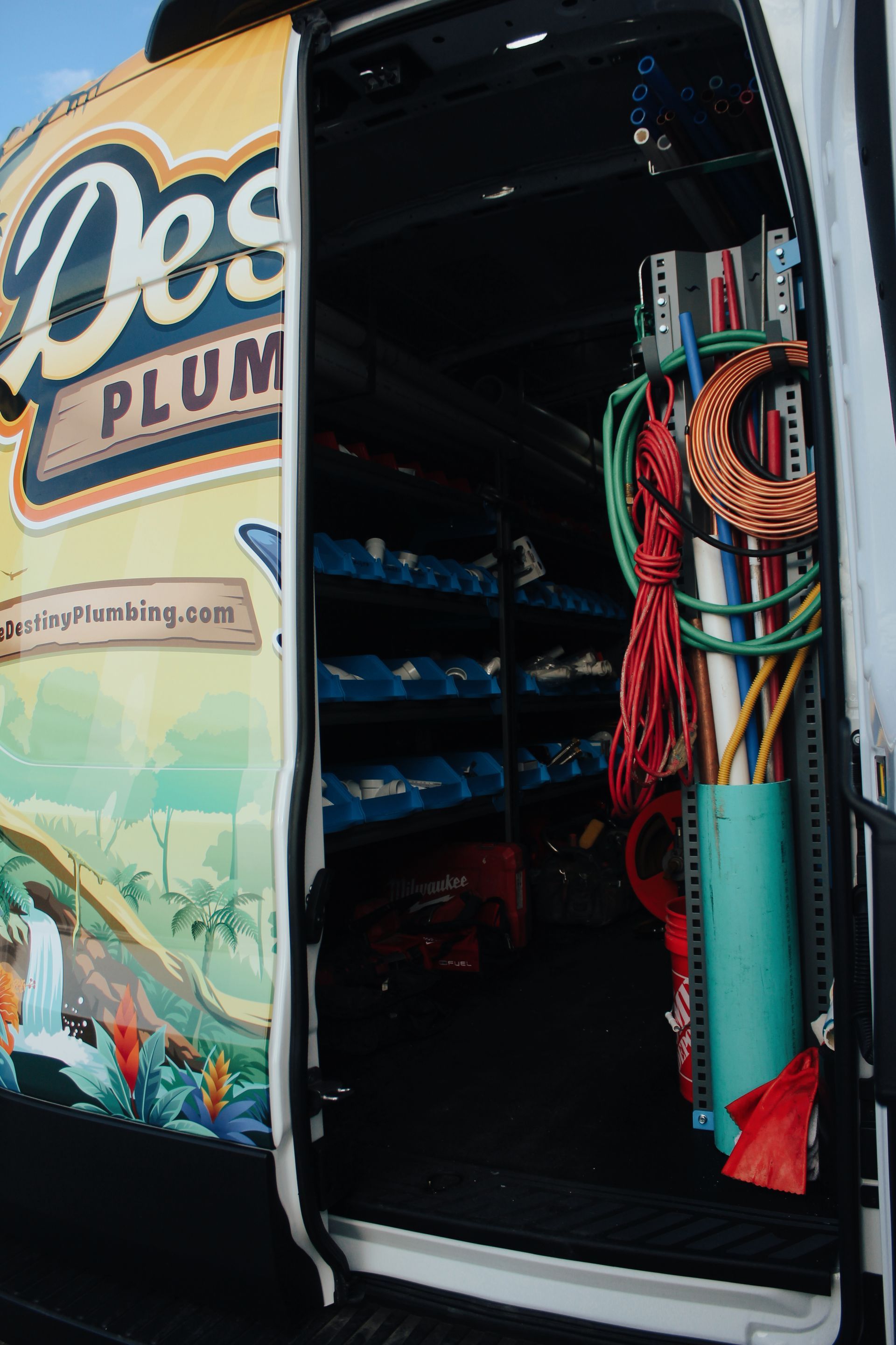 Open van with Destiny Plumbing logo and organized hoses and plumbing tools inside