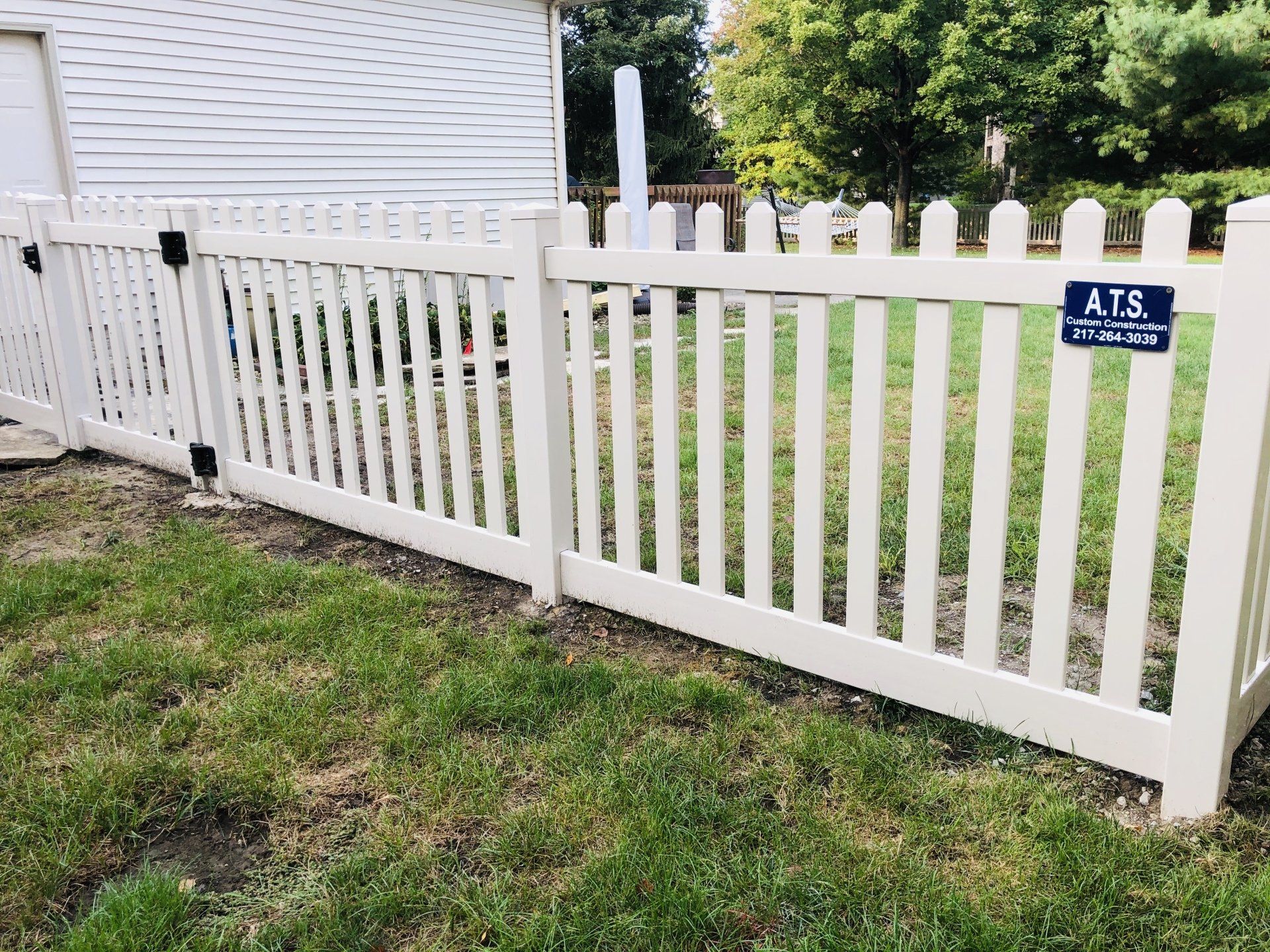 A white picket fence is sitting in the grass in front of a house.