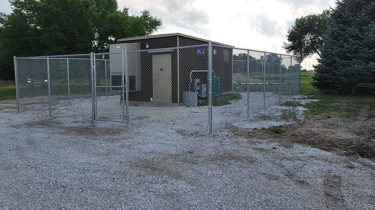 A chain link fence surrounds a building in a gravel area.