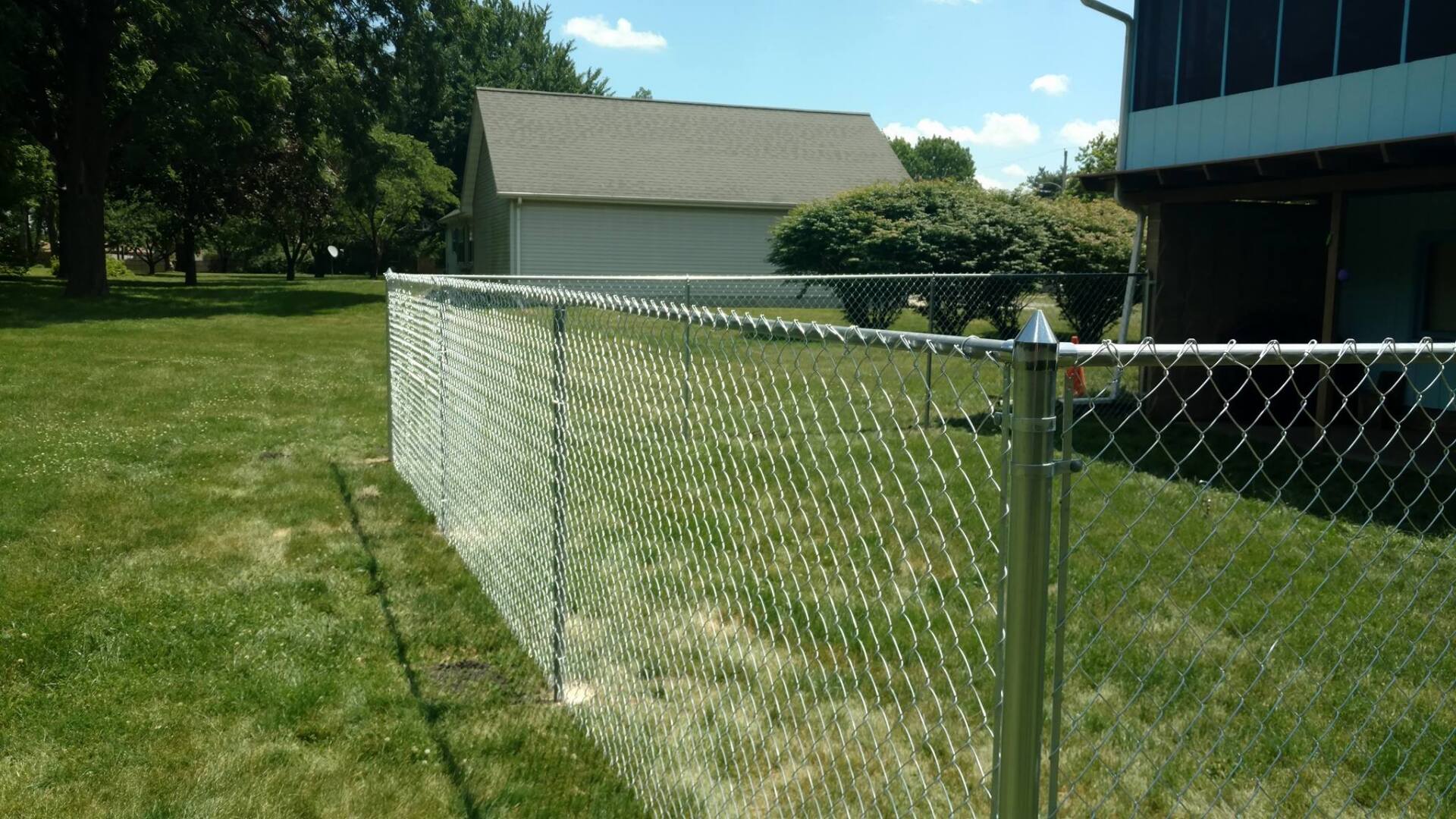 A chain link fence surrounds a lush green yard in front of a house.