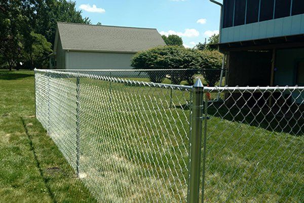 A chain link fence surrounds a lush green yard in front of a house.