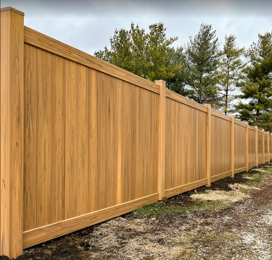 A wooden fence is sitting on the side of a dirt road.