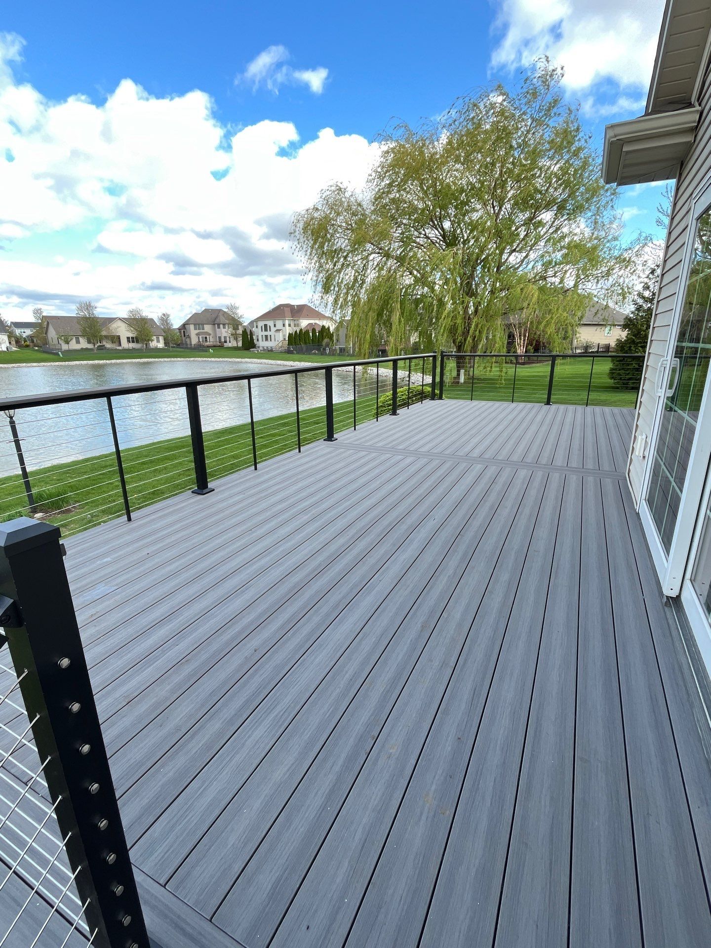 Gray composite deck overlooking a lake, with black railings and a tree in the background.