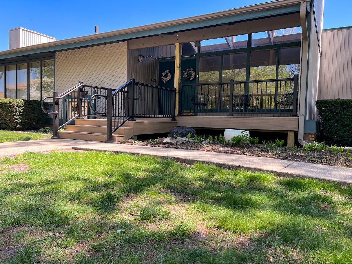 A house with a porch and stairs is sitting on top of a lush green field.