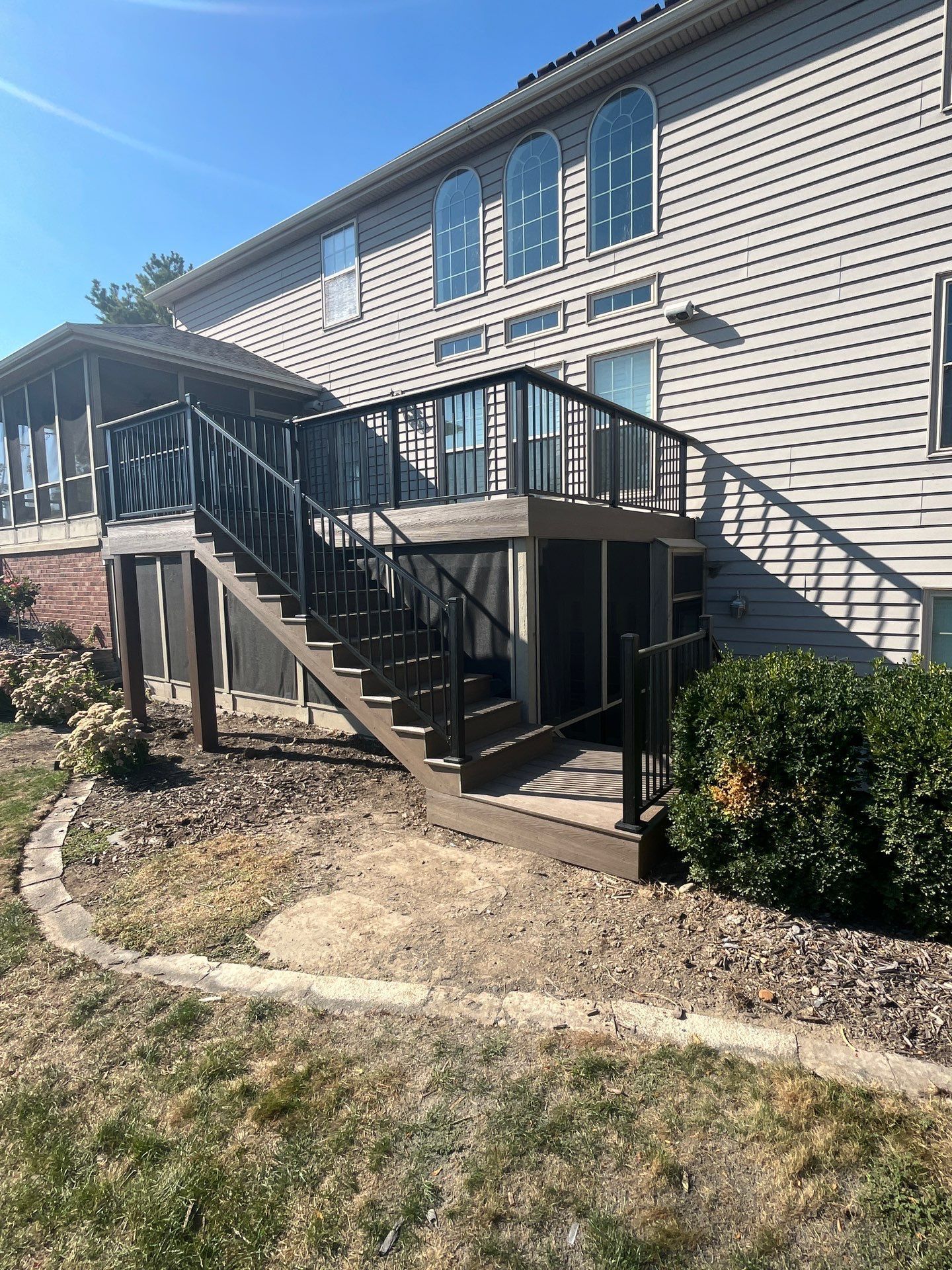 Backyard view of a two-story deck with steps, next to a house with arched windows.