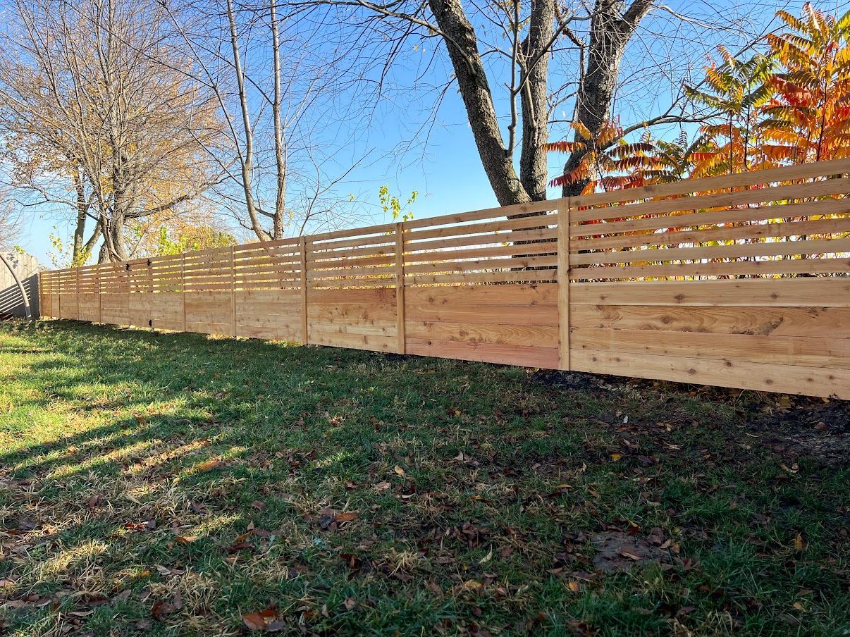 A wooden fence surrounds a lush green yard with trees in the background