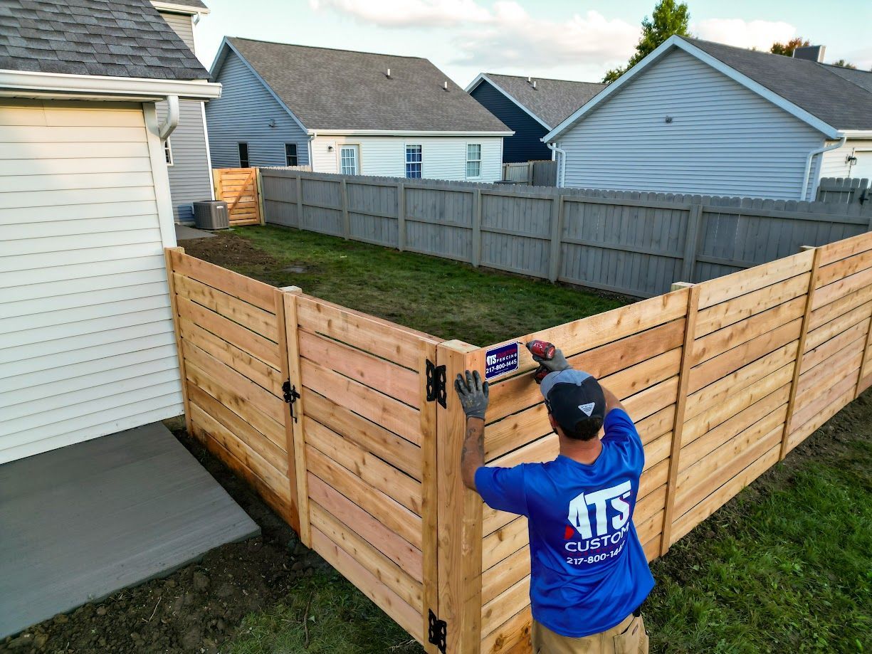 A man in a blue shirt is working on a wooden fence