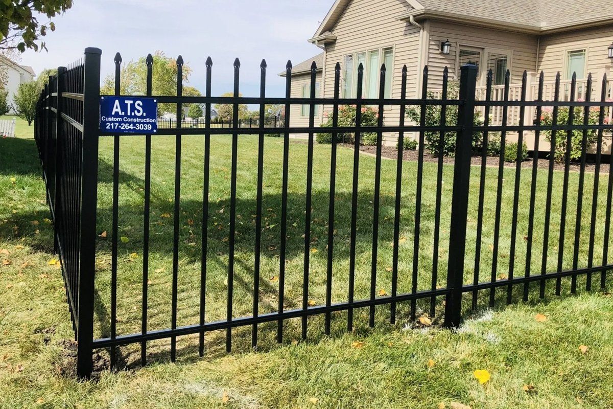 A black metal fence is sitting in the grass in front of a house.
