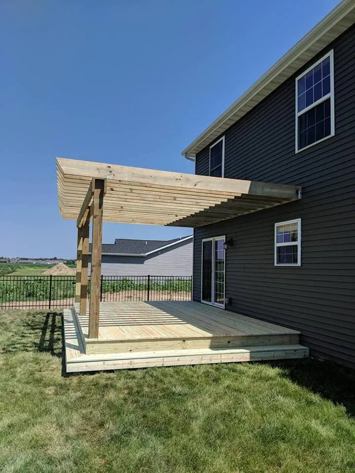 A wooden deck with a pergola attached to the side of a house.