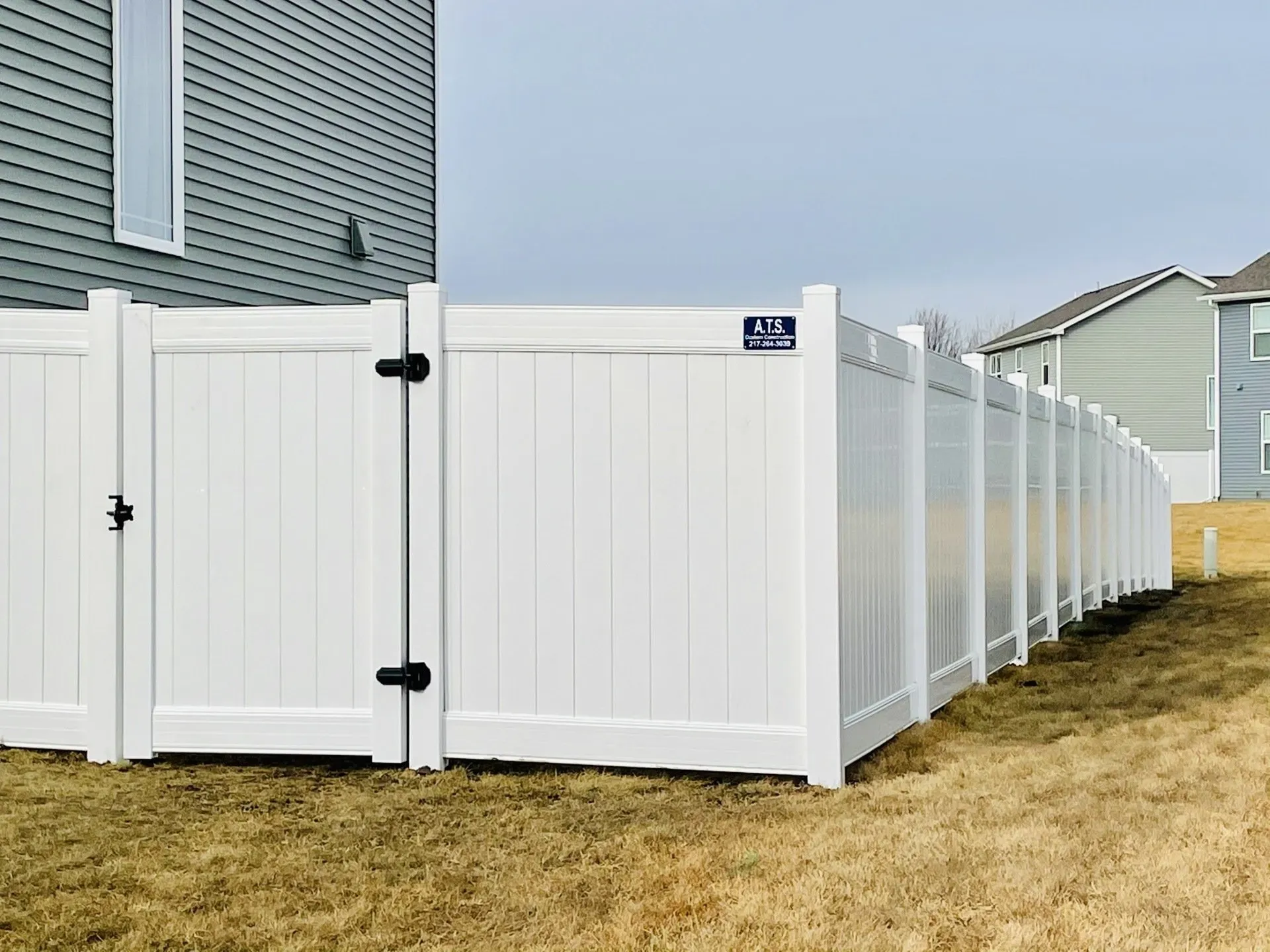 A white fence with a gate in the backyard of a house.