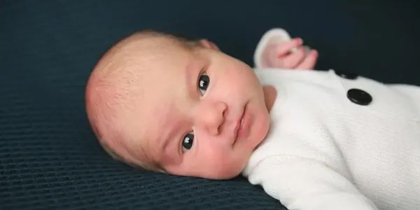 A baby is laying on a blue blanket and looking at the camera.