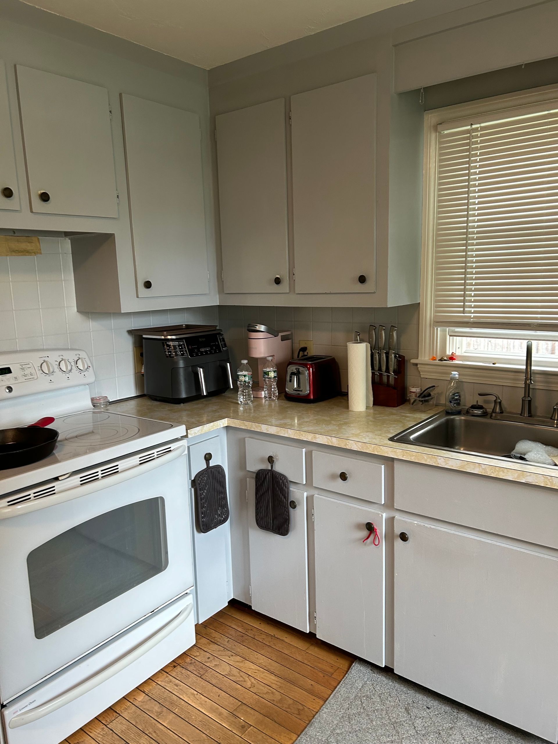 A kitchen with white cabinets , a stove , a sink , and a window.