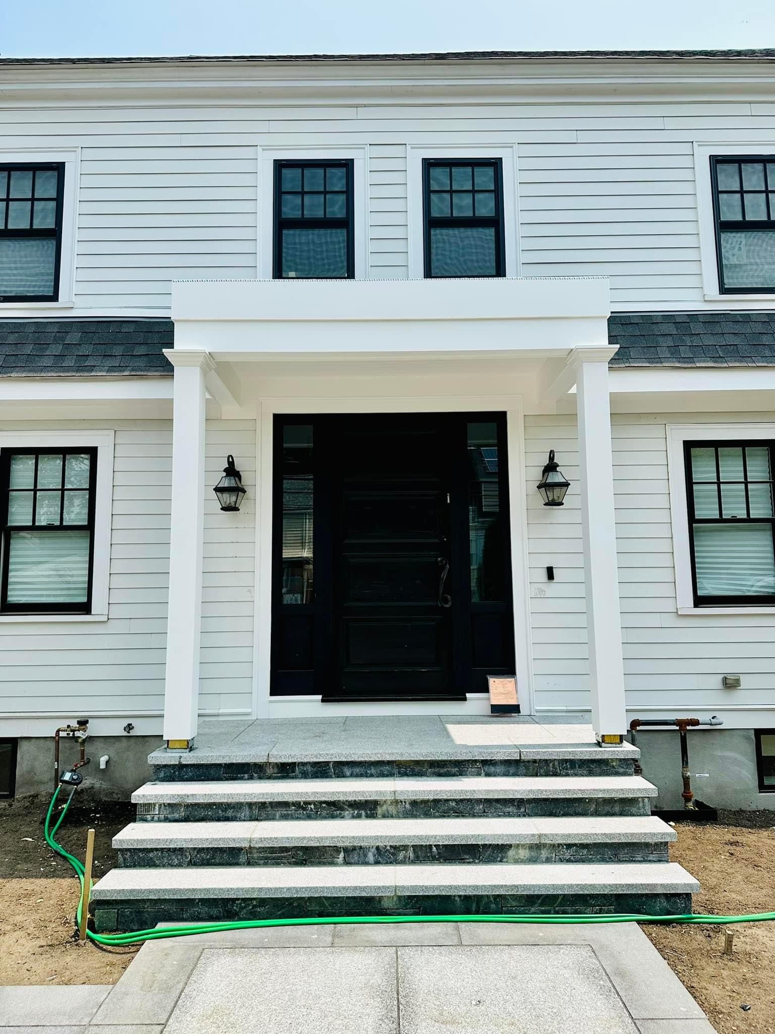 the front of a white house with black windows and a black door