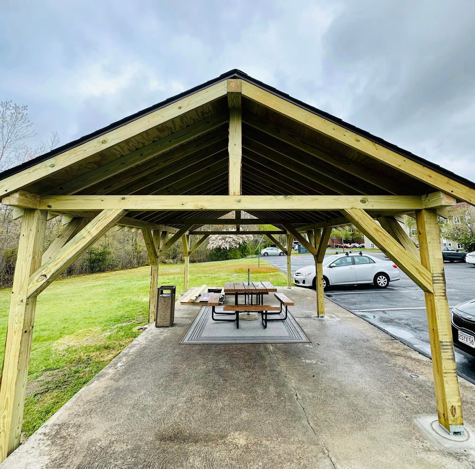 a picnic table is under a wooden structure in a parking lot