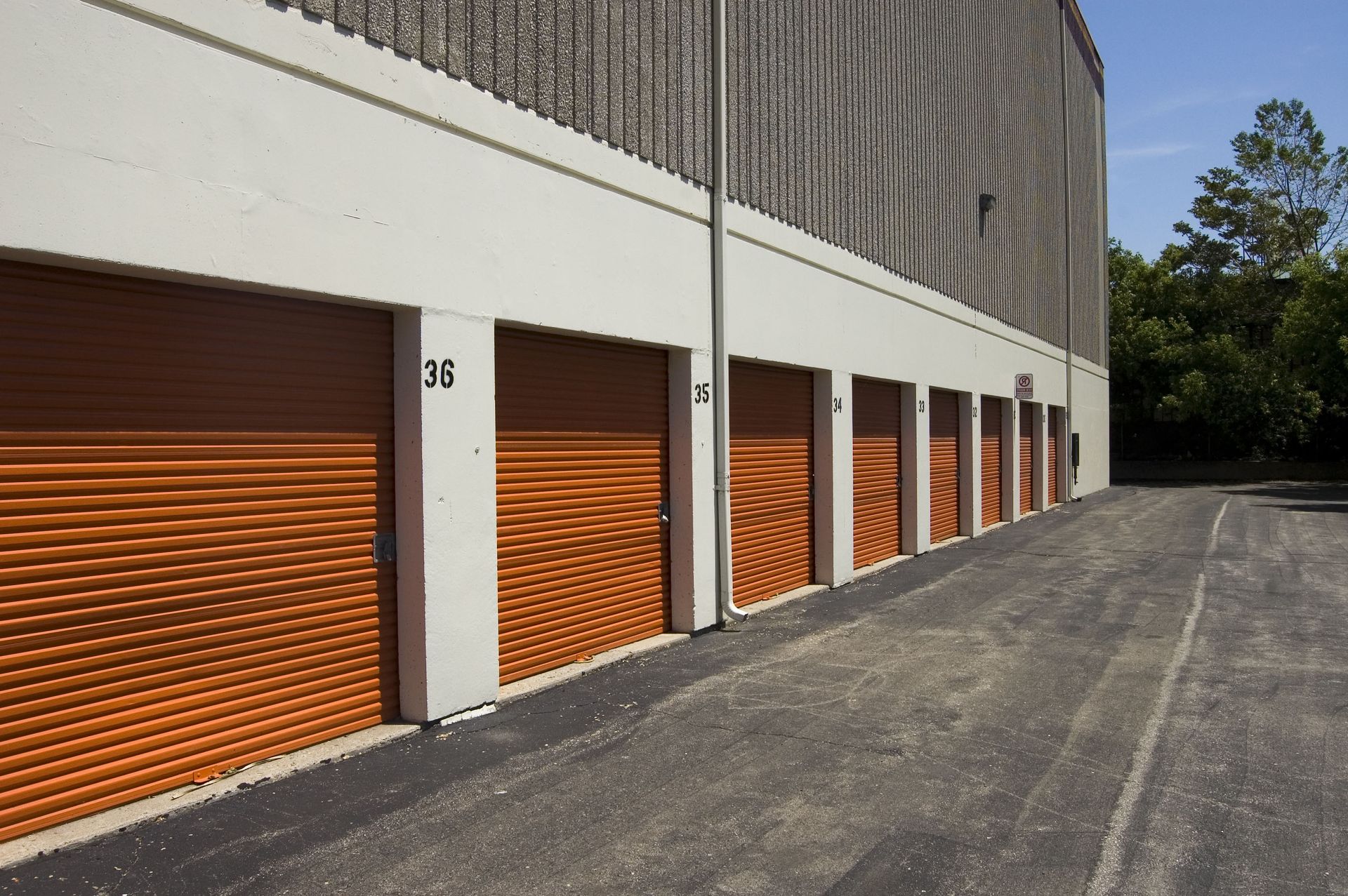 A row of orange roll-up storage unit doors numbered 33 through 38 along a concrete wall.