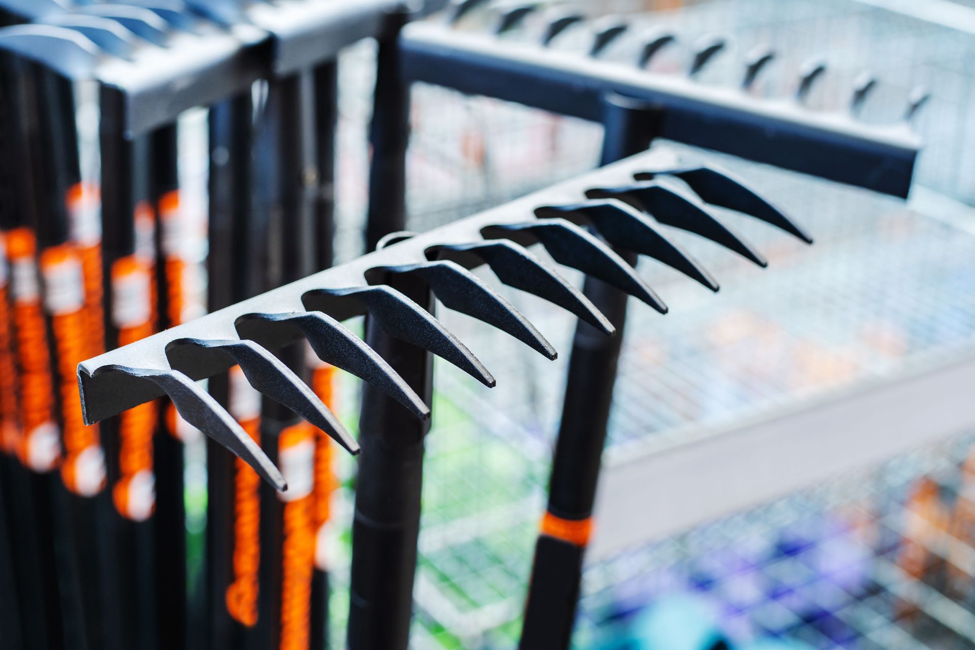 Close-up of black metal rakes with orange handles arranged in rows on a store display shelf.