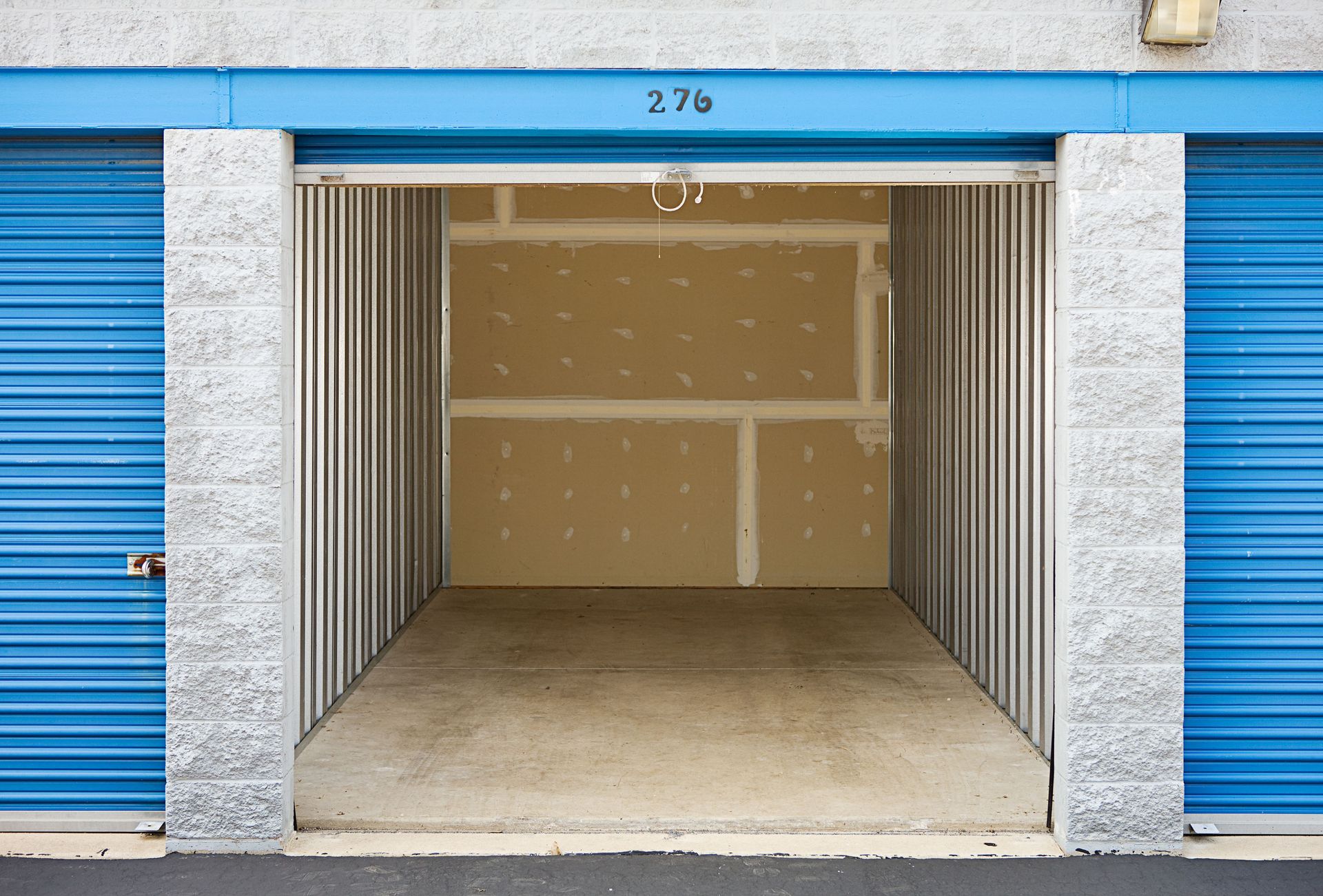 An open storage unit with blue metal doors and unpainted drywall interior walls, labeled 276.