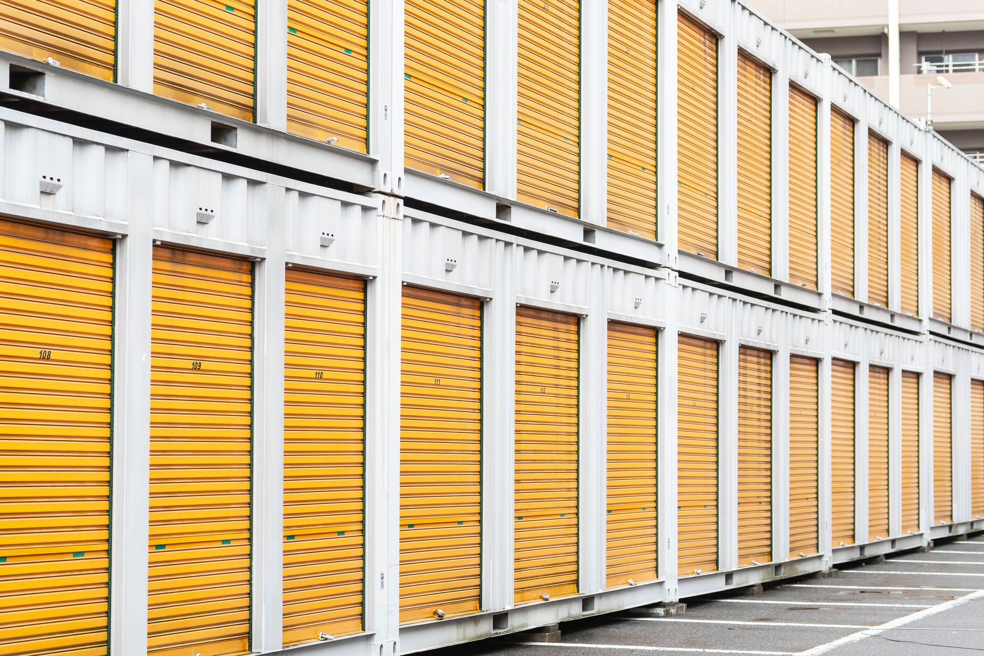 A two-story outdoor self-storage facility featuring multiple rows of closed, yellow roll-up metal doors.