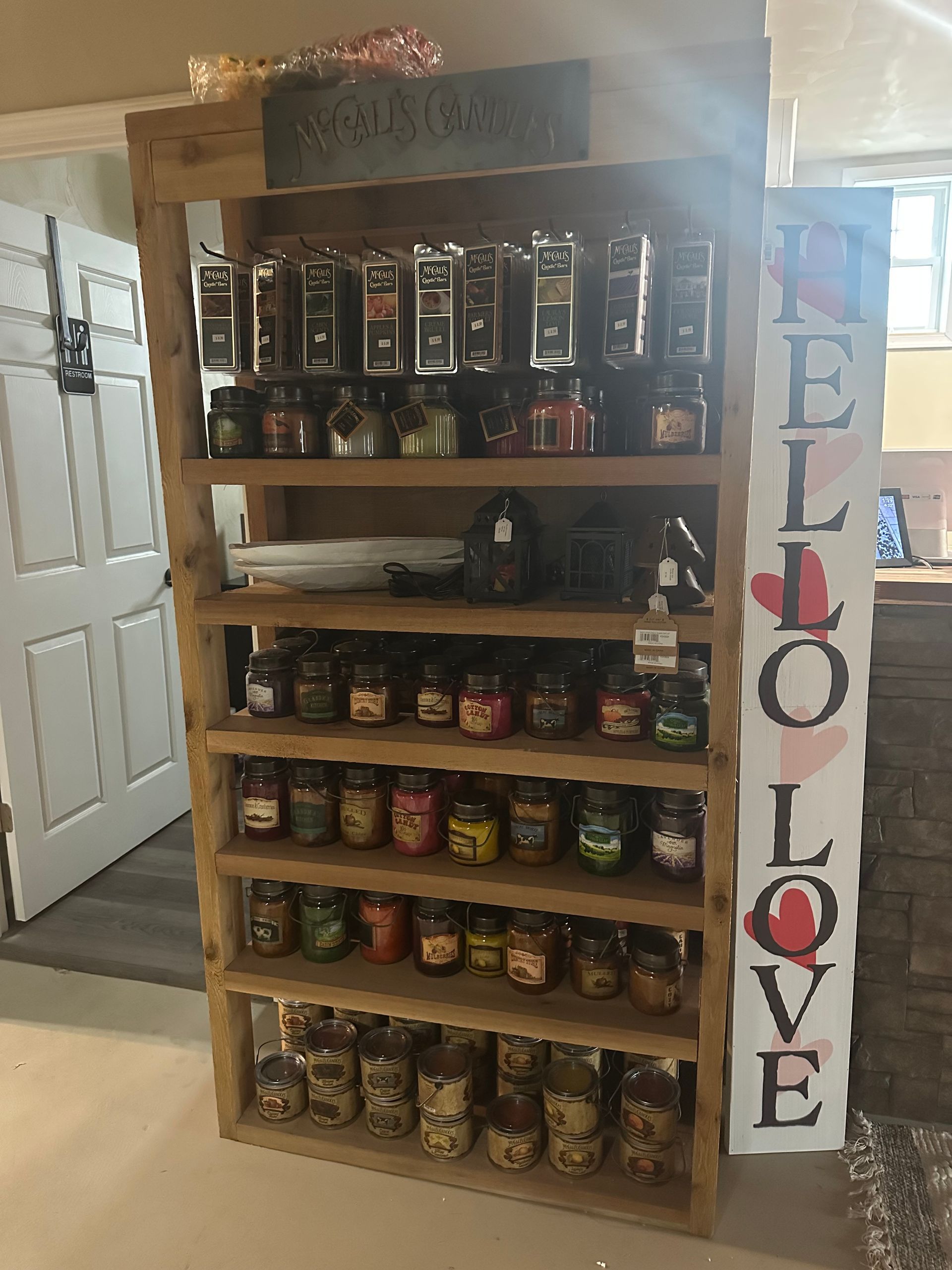 A wooden shelf filled with jars of candles and a sign that says