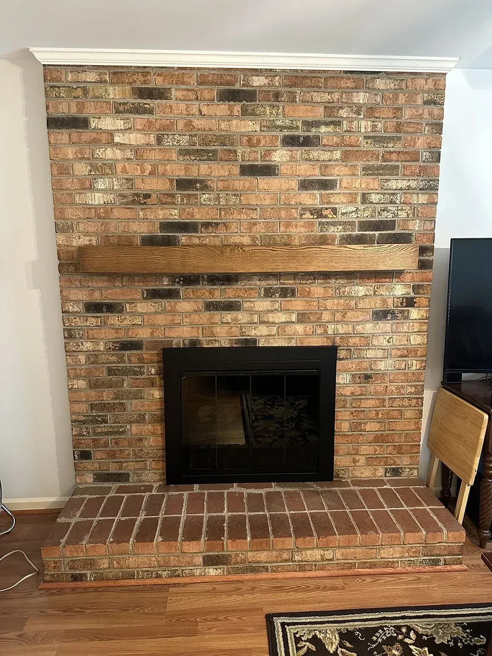 A living room with a brick fireplace and a wooden mantle.