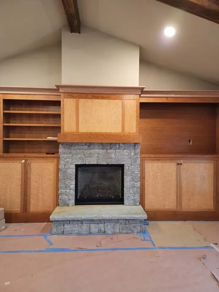 A living room with a stone fireplace and wooden cabinets