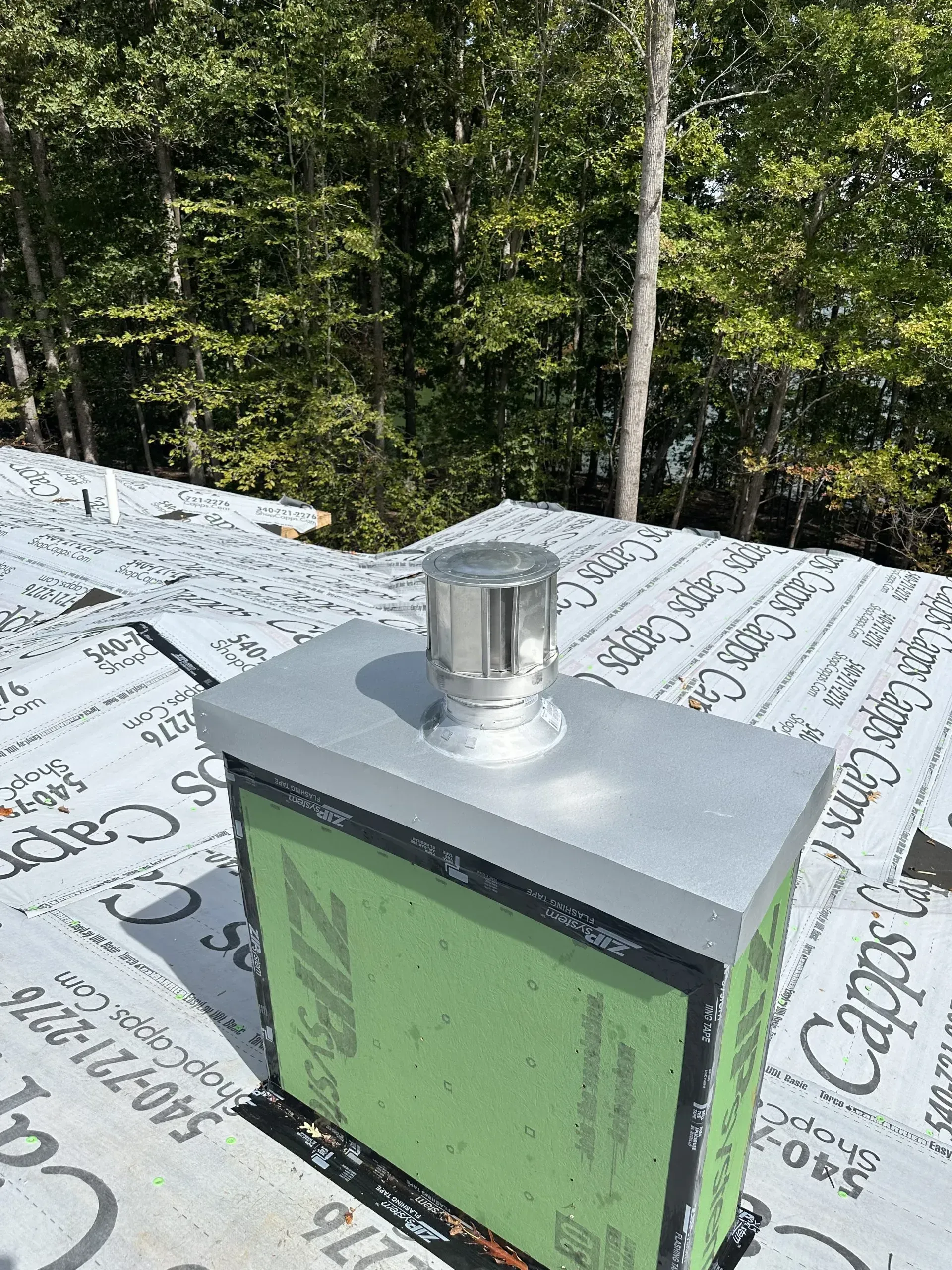 A chimney is sitting on top of a roof with trees in the background.