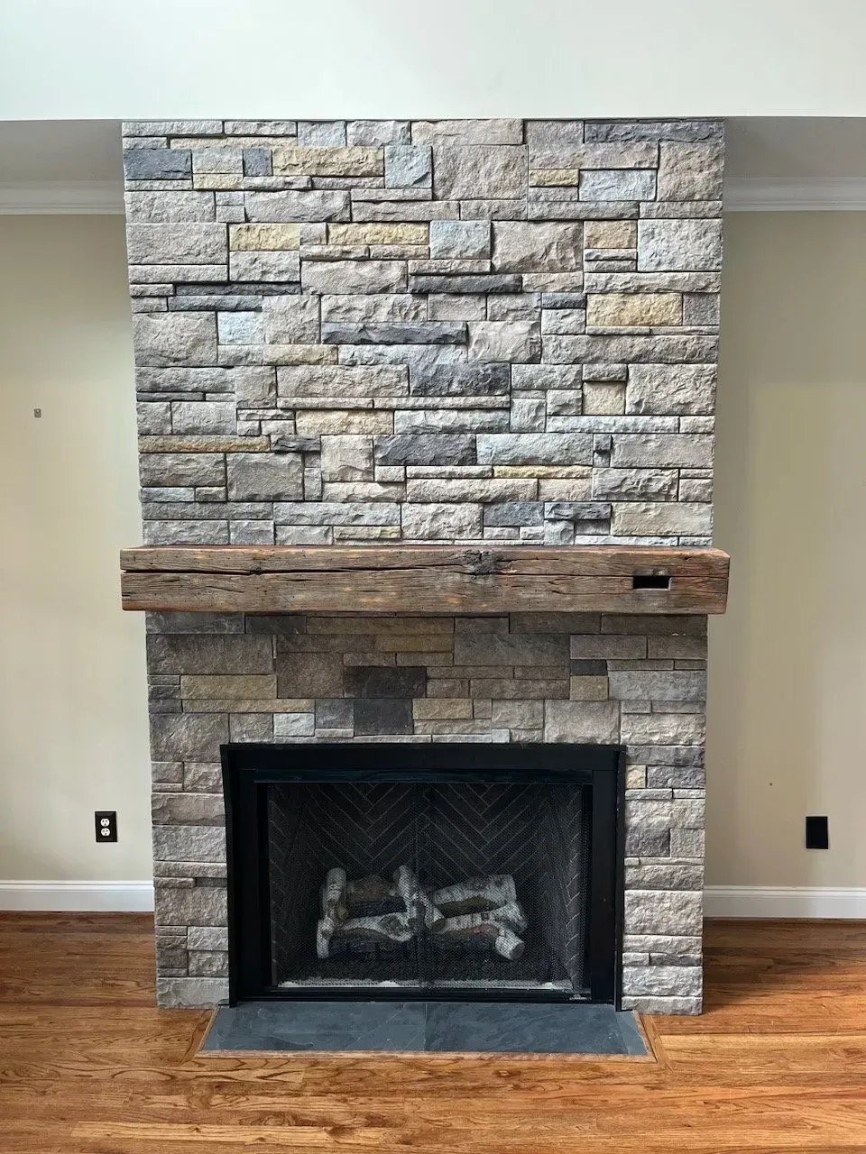 A fireplace with a stone wall and a wooden mantle in a living room.