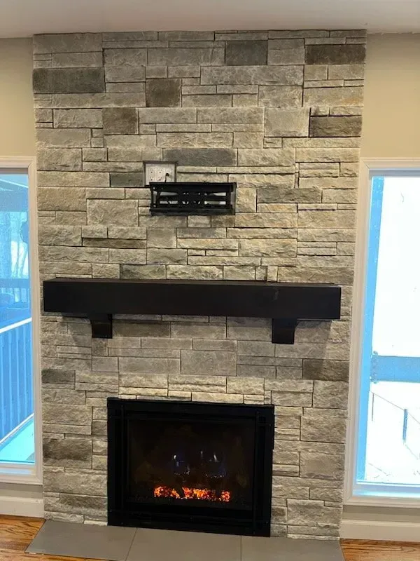 A fireplace with a stone wall and a mantle in a living room.